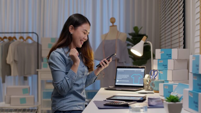 Ecstatic female entrepreneur in front of computer in clothing shop.